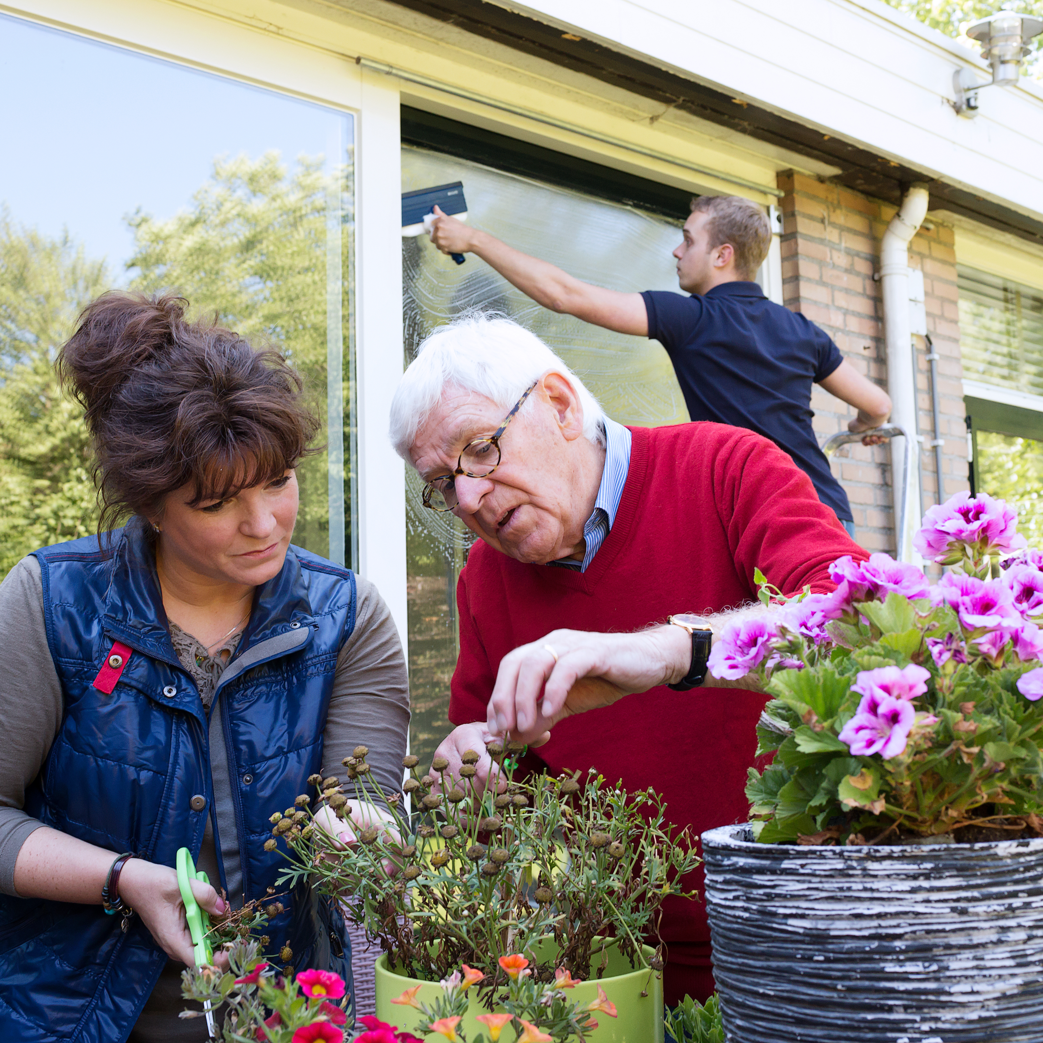 meneer verzorgt plantjes met dochter terwijl glazenwasser ramen wast